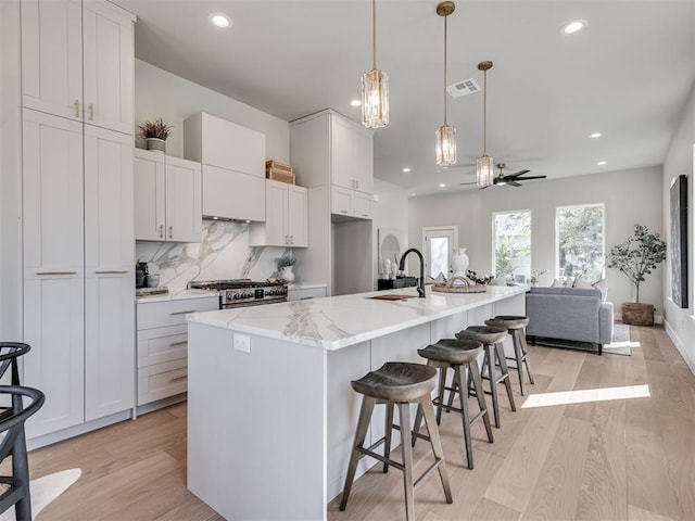 12 S Howard St, Edmond, OK 73003 - kitchen featuring visible vents, tasteful backsplash, light wood-style floors, and stainless steel range with gas stovetop