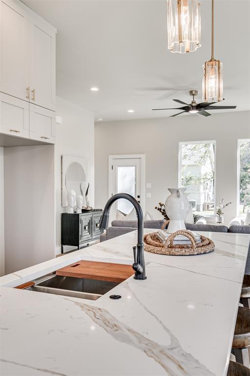 12 S Howard St, Edmond, OK 73003 - kitchen with light stone counters, ceiling fan with notable chandelier, white cabinets, and a sink