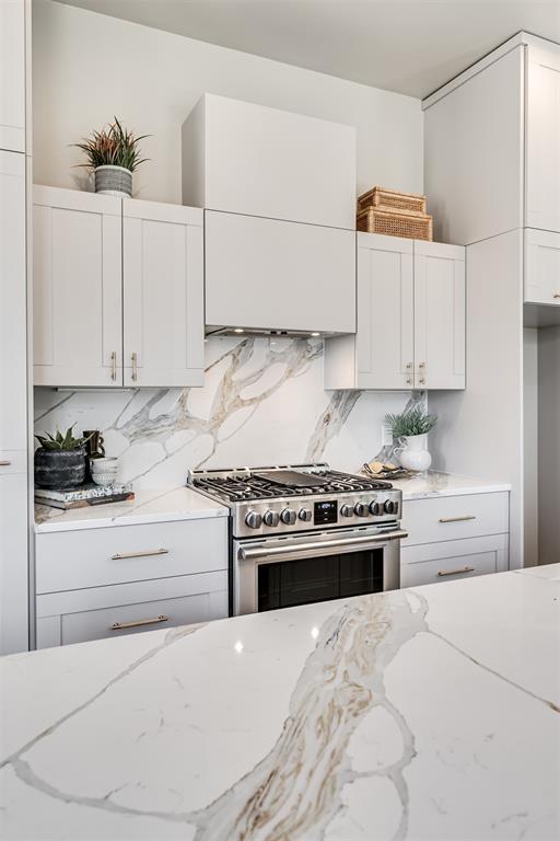 12 S Howard St, Edmond, OK 73003 - kitchen with decorative backsplash, stainless steel range with gas stovetop, and white cabinetry