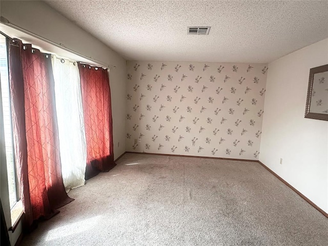 carpeted spare room with visible vents, baseboards, a textured ceiling, and wallpapered walls