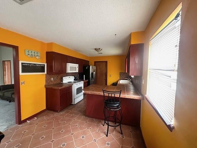 kitchen with tile countertops, a breakfast bar area, a peninsula, white appliances, and a sink