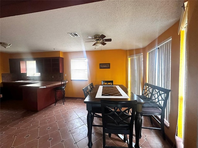 dining space featuring a textured ceiling, dark tile patterned flooring, visible vents, and ceiling fan