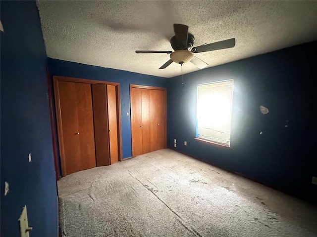 unfurnished bedroom with a textured ceiling, two closets, a ceiling fan, and carpet