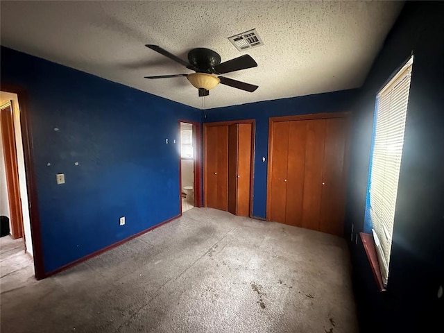 unfurnished bedroom with a ceiling fan, visible vents, carpet floors, a textured ceiling, and two closets