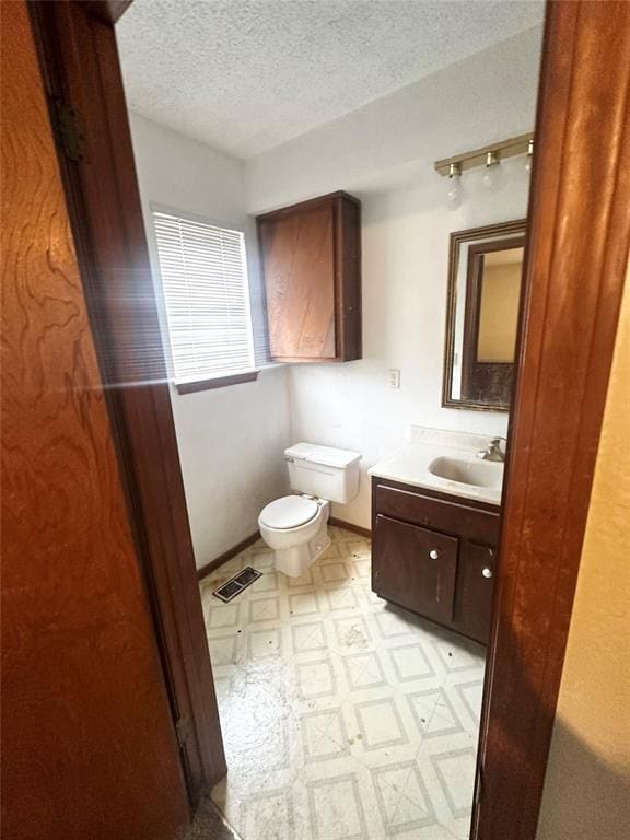 half bath with tile patterned floors, visible vents, toilet, a textured ceiling, and vanity