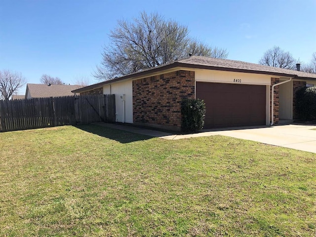 view of side of property featuring brick siding, a lawn, an attached garage, and fence