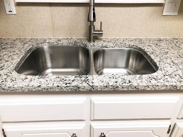 room details with white cabinetry, light stone countertops, and a sink