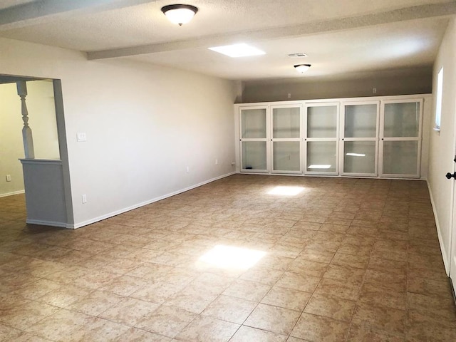 spare room featuring visible vents, baseboards, a textured ceiling, and beam ceiling