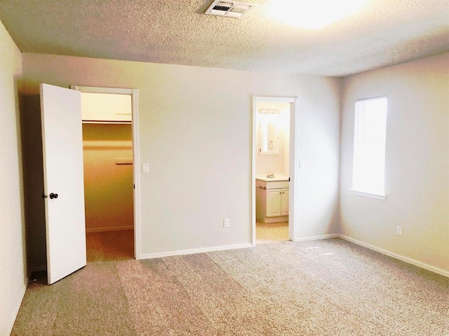 unfurnished bedroom featuring visible vents, a walk in closet, a textured ceiling, connected bathroom, and carpet