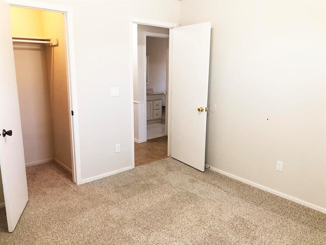 unfurnished bedroom with a closet, light carpet, baseboards, and a spacious closet