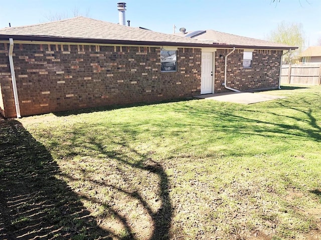 rear view of house featuring a patio, fence, a yard, roof with shingles, and brick siding