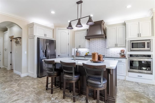 kitchen featuring a breakfast bar area, custom exhaust hood, arched walkways, ornamental molding, and appliances with stainless steel finishes