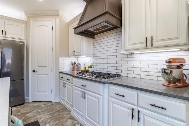 kitchen with tasteful backsplash, premium range hood, dark stone counters, white cabinets, and stainless steel appliances