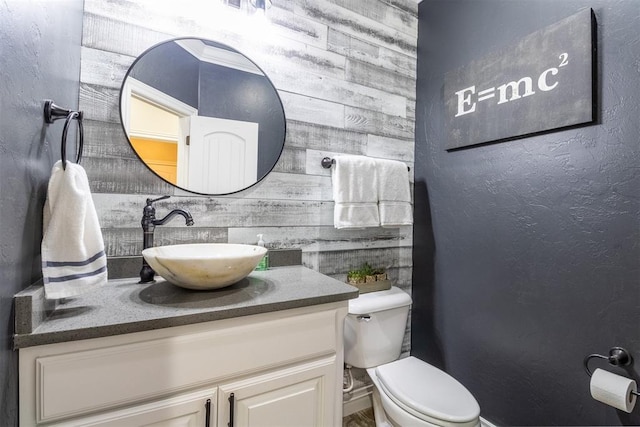 half bathroom featuring toilet, vanity, and a textured wall