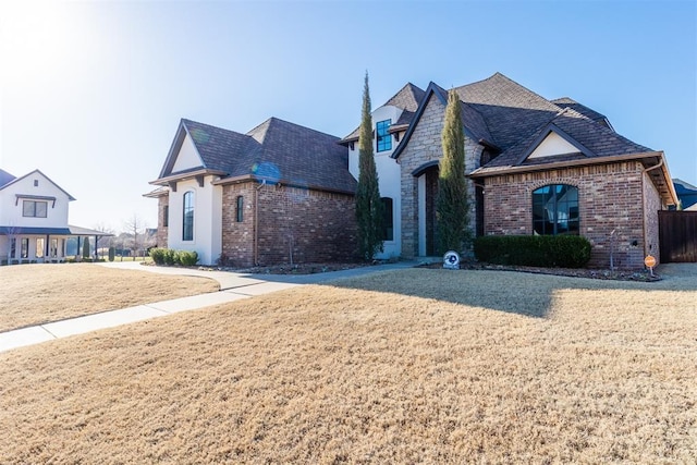 french country style house featuring a front yard, brick siding, and stone siding