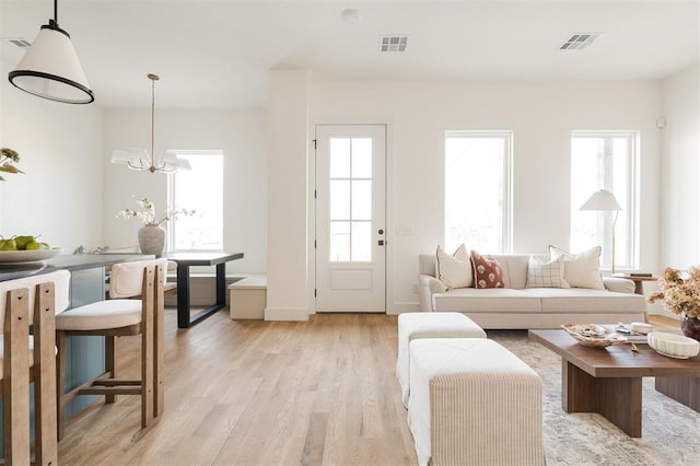living area with light wood-type flooring, visible vents, and an inviting chandelier