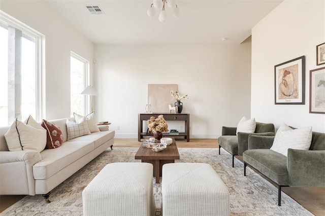 living room featuring visible vents, baseboards, light wood-style floors, and an inviting chandelier