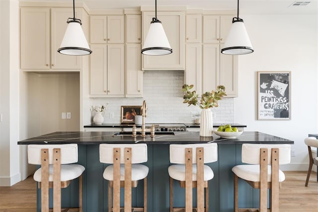 kitchen featuring light wood-style floors, decorative backsplash, dark countertops, and visible vents
