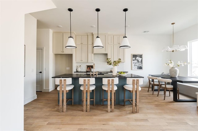 kitchen with dark countertops, decorative backsplash, light wood finished floors, and an island with sink