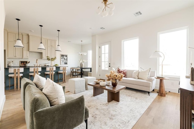 living room with visible vents, baseboards, a notable chandelier, and light wood-style flooring