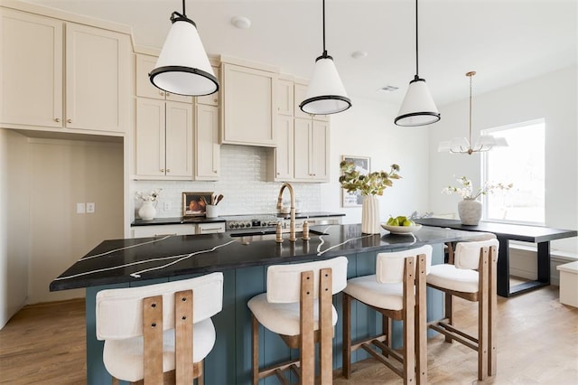 kitchen with dark countertops, visible vents, backsplash, light wood finished floors, and a sink