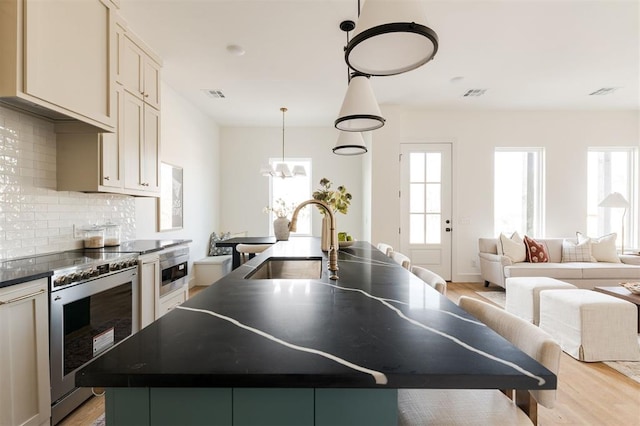 kitchen featuring visible vents, a center island with sink, a sink, dark countertops, and stainless steel range with electric cooktop