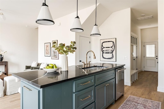 kitchen with light wood-style flooring, a center island with sink, a sink, dark countertops, and dishwasher
