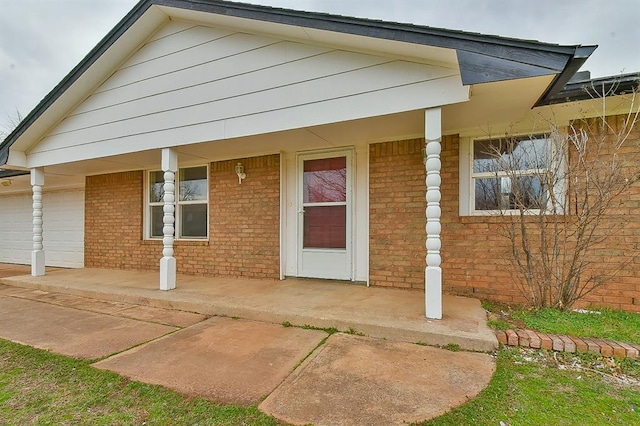 exterior space featuring a porch, an attached garage, and brick siding