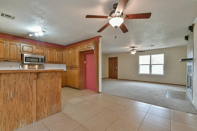 kitchen with visible vents, light carpet, brown cabinets, stainless steel microwave, and a peninsula