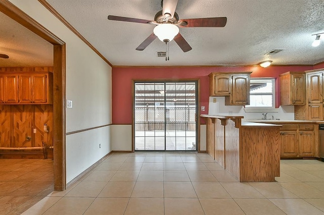 kitchen featuring light tile patterned floors, ornamental molding, brown cabinetry, and light countertops