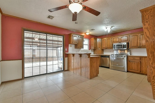 kitchen with visible vents, brown cabinets, stainless steel appliances, a peninsula, and light countertops