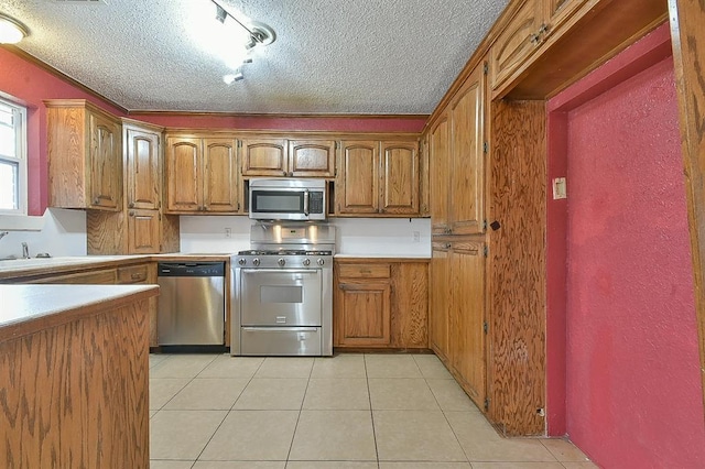 kitchen featuring light tile patterned floors, brown cabinetry, a sink, stainless steel appliances, and a textured ceiling