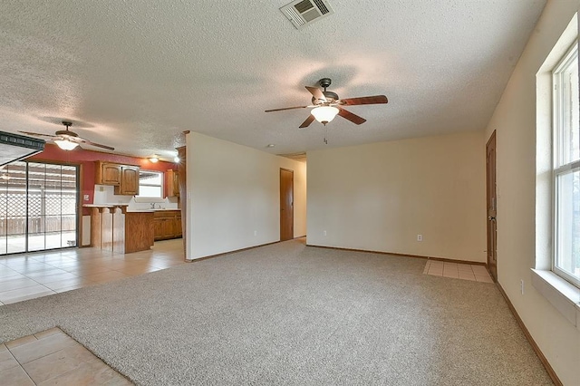 unfurnished living room with visible vents, light carpet, a ceiling fan, a textured ceiling, and baseboards