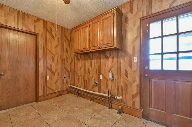 clothes washing area featuring wooden walls, gas dryer hookup, cabinet space, electric dryer hookup, and a textured ceiling