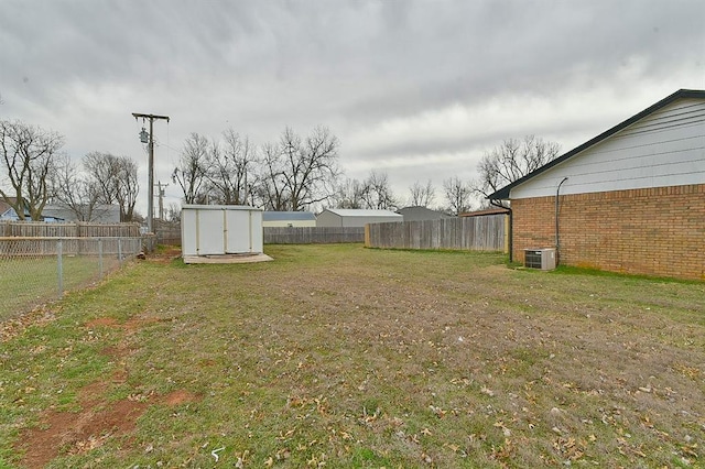 view of yard featuring a storage unit, central air condition unit, an outbuilding, and a fenced backyard