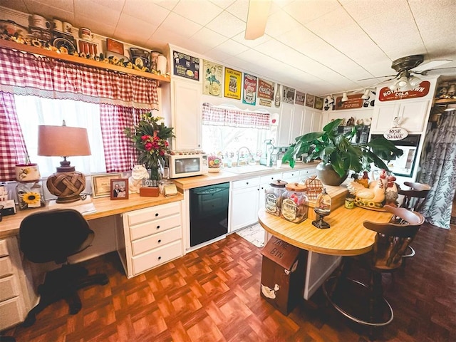 kitchen with white microwave, ceiling fan, dishwasher, built in study area, and a sink