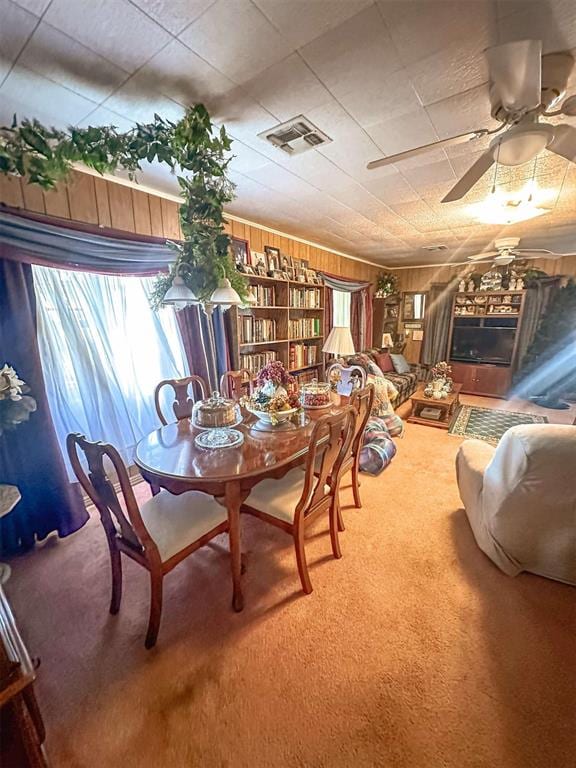 dining area with carpet, visible vents, wood walls, and ceiling fan