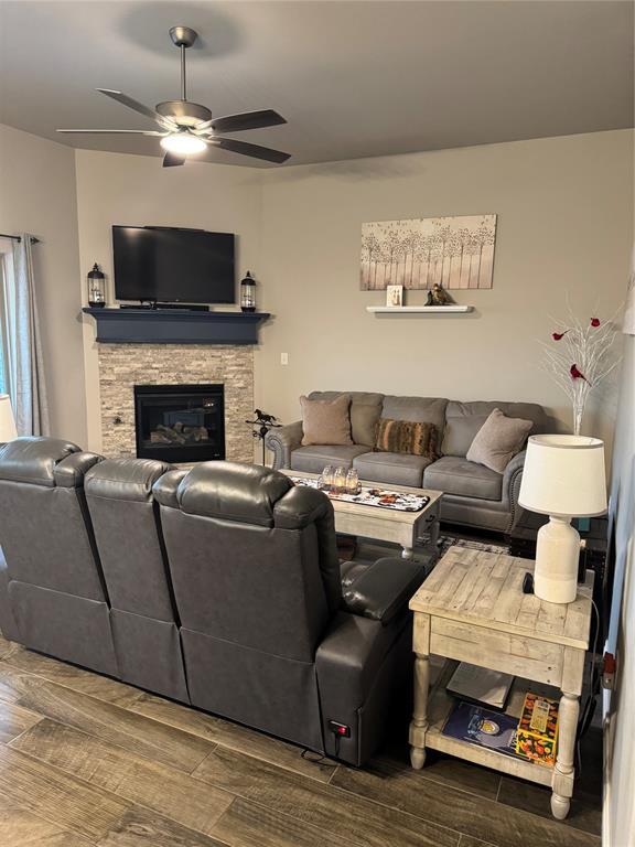 living area featuring a stone fireplace, wood finished floors, and a ceiling fan