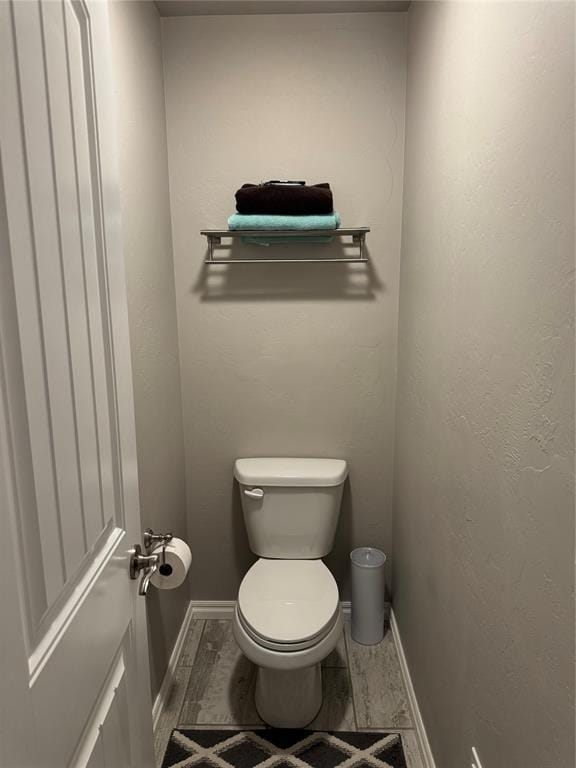 bathroom with a textured wall, toilet, baseboards, and wood finished floors