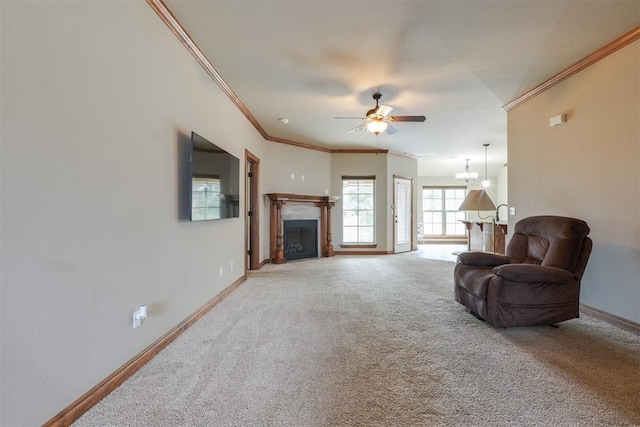 living area featuring baseboards, crown molding, carpet flooring, and ceiling fan with notable chandelier