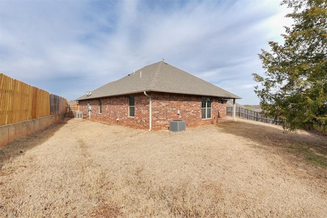 rear view of house featuring brick siding, central AC, a fenced backyard, and a shingled roof