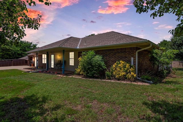 back of property at dusk with a patio area, brick siding, a lawn, and fence