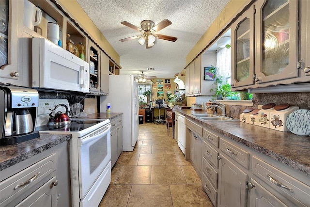 kitchen featuring a ceiling fan, a sink, dark countertops, a textured ceiling, and white appliances