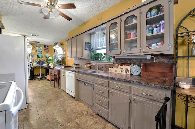 kitchen with a ceiling fan, gray cabinets, a sink, dark countertops, and white appliances