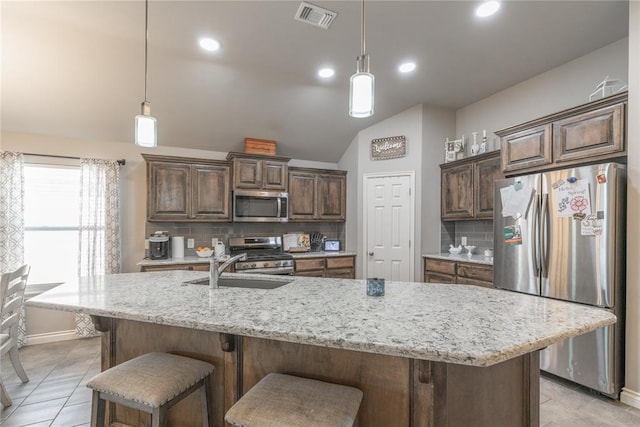 kitchen featuring visible vents, a sink, stainless steel appliances, light stone countertops, and vaulted ceiling