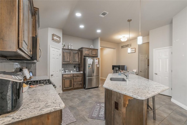 kitchen featuring visible vents, a breakfast bar, an island with sink, a sink, and appliances with stainless steel finishes