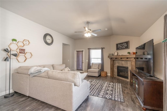 living room with a ceiling fan, baseboards, dark wood finished floors, a tile fireplace, and vaulted ceiling