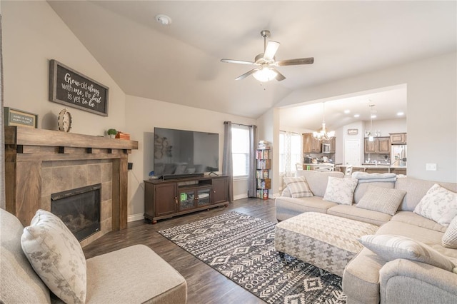 living area featuring baseboards, a fireplace, dark wood-style flooring, vaulted ceiling, and ceiling fan with notable chandelier