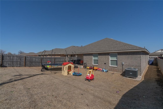 back of house with a trampoline, a fenced backyard, cooling unit, a shingled roof, and brick siding