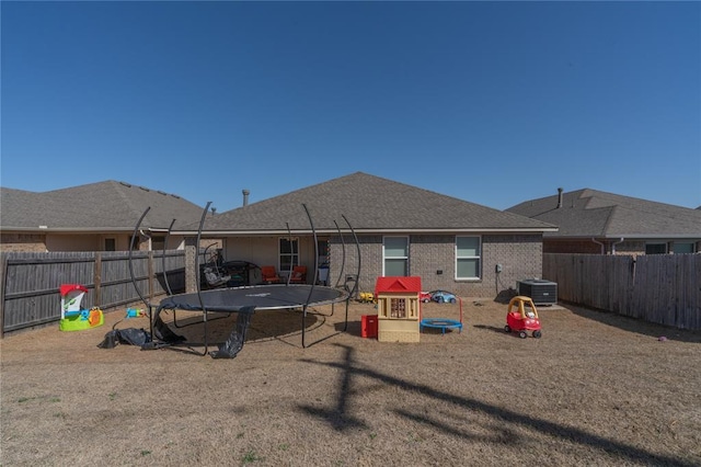 rear view of house featuring a fenced backyard, central air condition unit, brick siding, and a trampoline